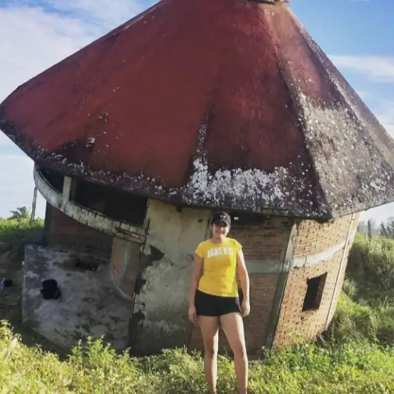 Una turista sonriendo frente a la fachada de la famosa Casa Chueca, una llamativa estructura inclinada y uno de los atractivos turísticos más curiosos que visitar en Tecolutla, Veracruz.